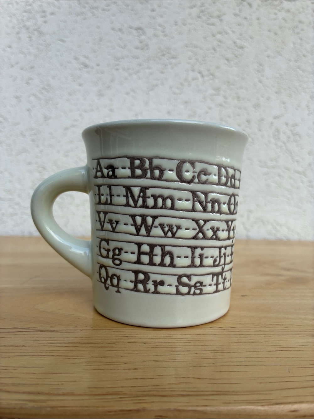 Ceramic Alphabet Mug in Cream with brown script on handwriting practice lines
